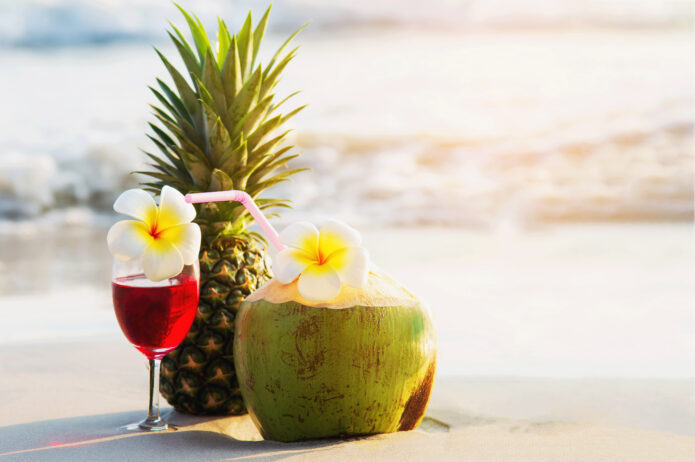 cocktail-glasses-with-coconut-and-pineapple-on-clean-sand-beach-fruit-and-drink-on-sea-beach