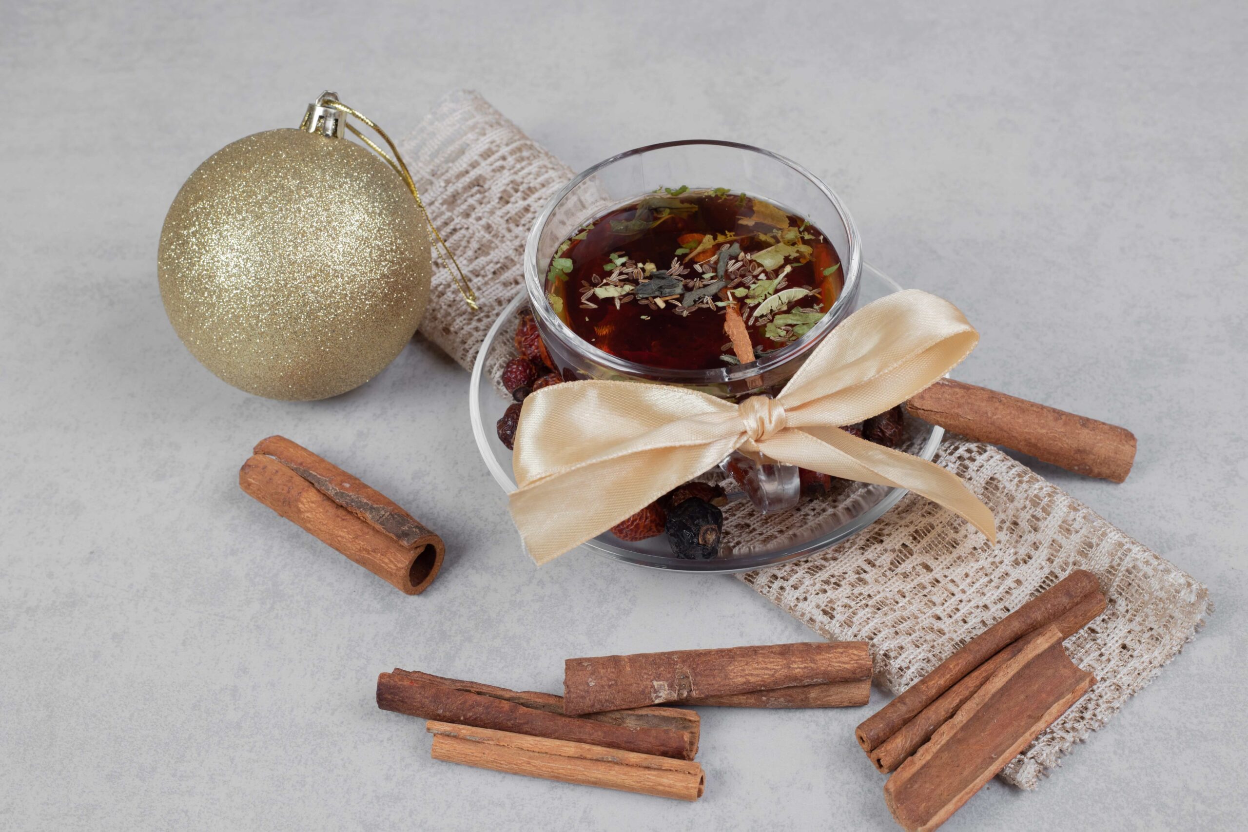 cup-of-tea-cinnamon-sticks-and-festive-ball-on-white-table-high-quality-photo-min (1)
